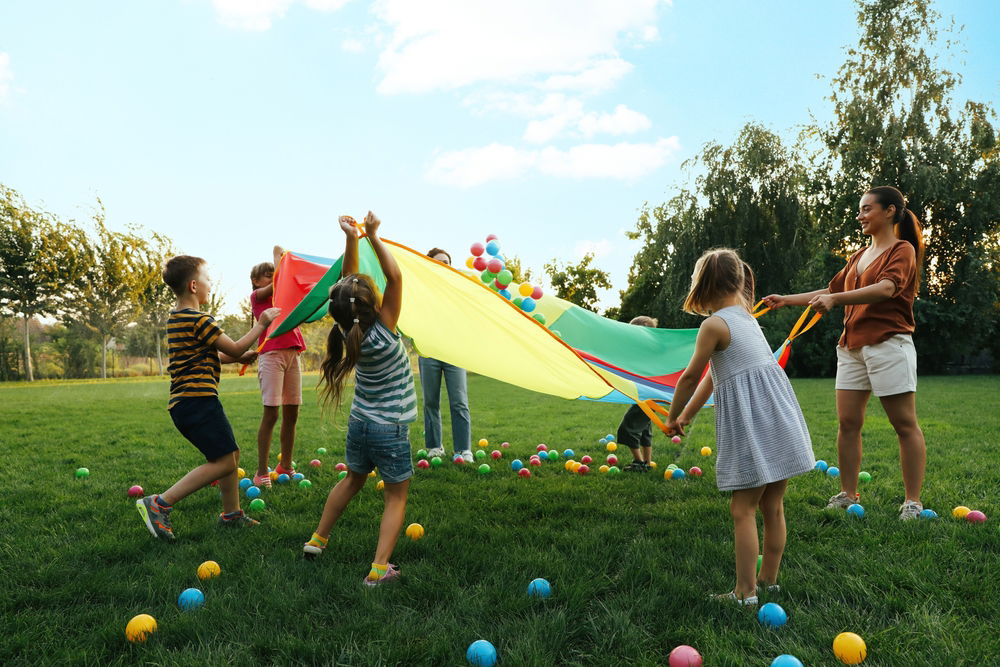 Children and teacher playing with a parachute and balls on a playground at a Saratoga Springs school 